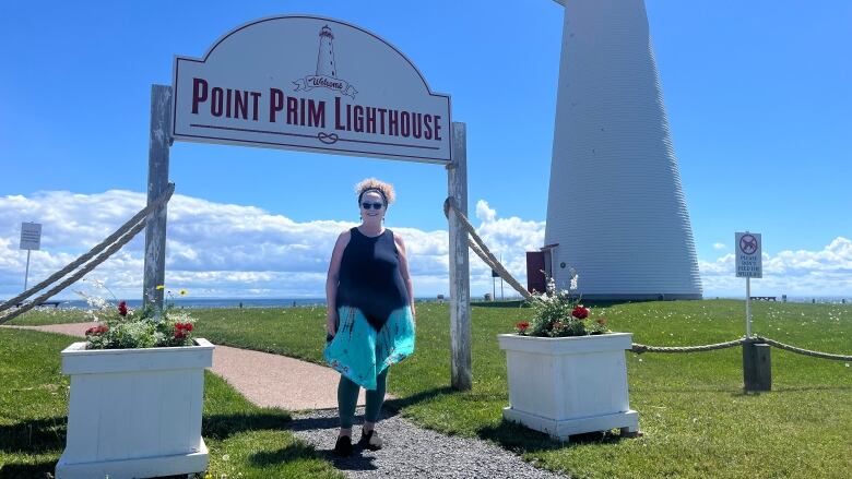 A woman stands in front of a lighthouse 