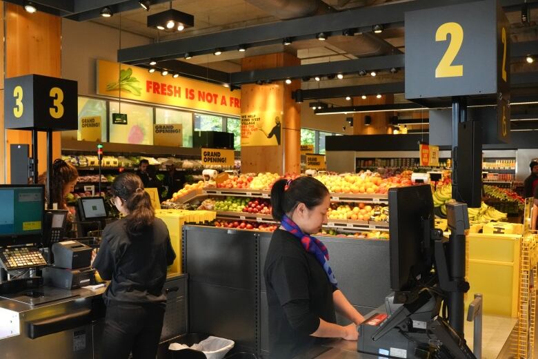 Two women wearing black stand at a grocery store checkout counter.