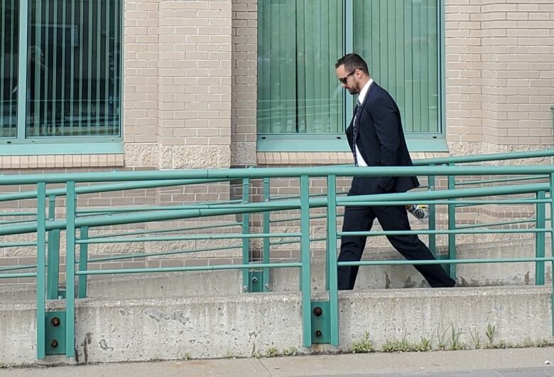 Seen from a distance, a bearded, dark-haired man in a suit looks down as he walks down a ramp from the Prince George courthouse, where he is on trial for obstruction of justice. 