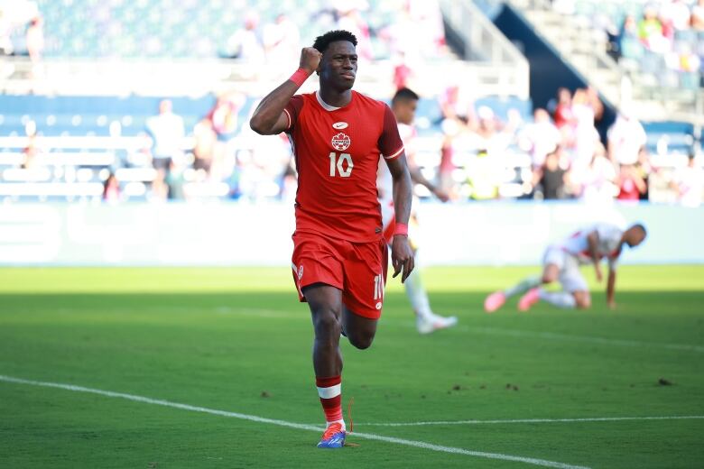 A male soccer player wearing number 10 pumps his right fist in celebration while running on the field.