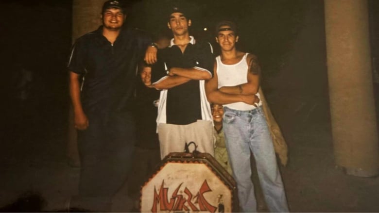 An old photograph shows three young men standing in front of a drum that says Muskrat in red lettering.