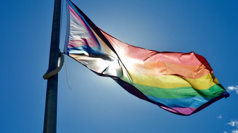 A Pride flag flapping against a backdrop of blue sky