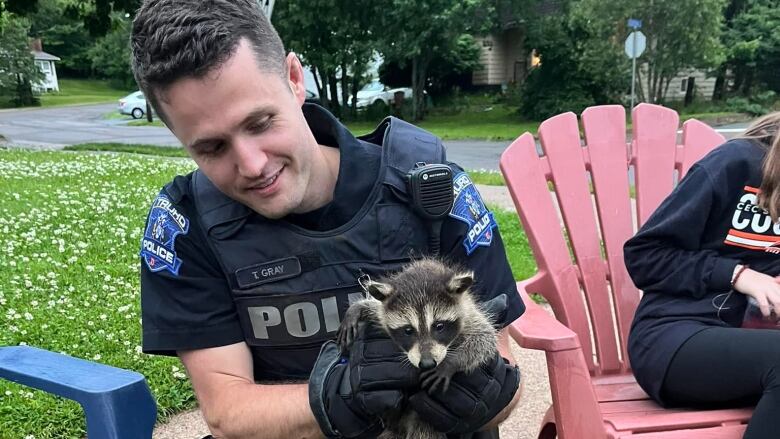 Man in police uniform holds raccoon.