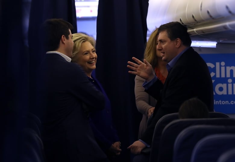 Hillary Clinton talks to a man in a suit on a plane