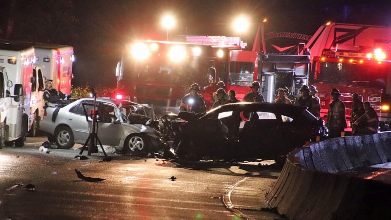 Two badly damaged cars with firefighters around them. 