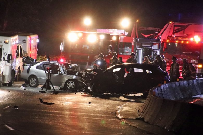 Two badly damaged cars with firefighters around them. 