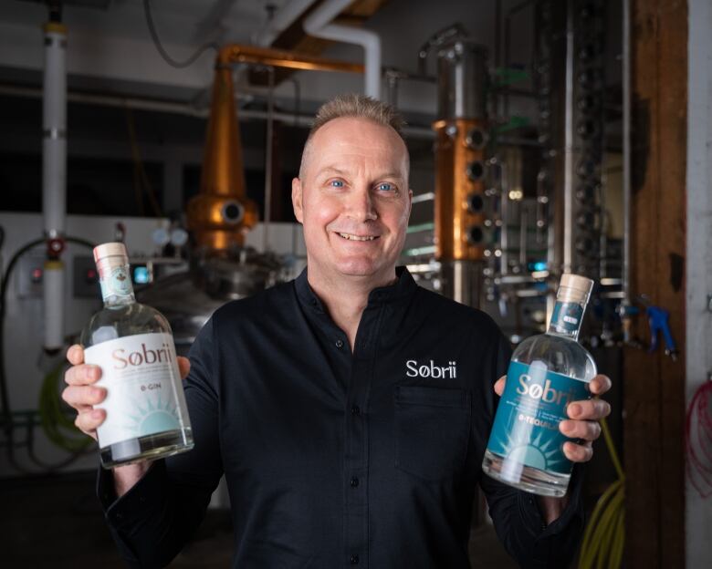 A man holds two bottles of zero-proof gin.