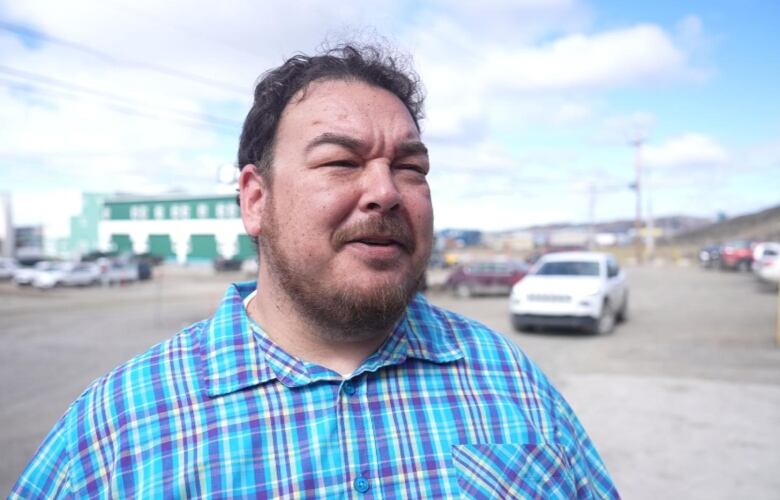 A man in a plaid shirt speaks outside 