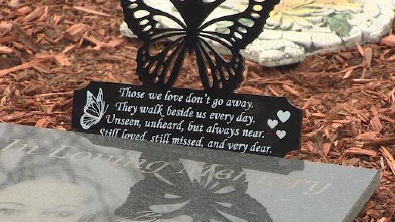 A butterfly sits atop a memorial stone with a photo of a young woman's face etched onto it. 