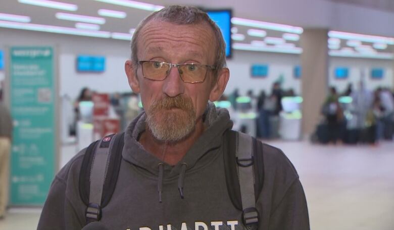 A man wearing glasses and a hoodie is pictured speaking in front of a camera.