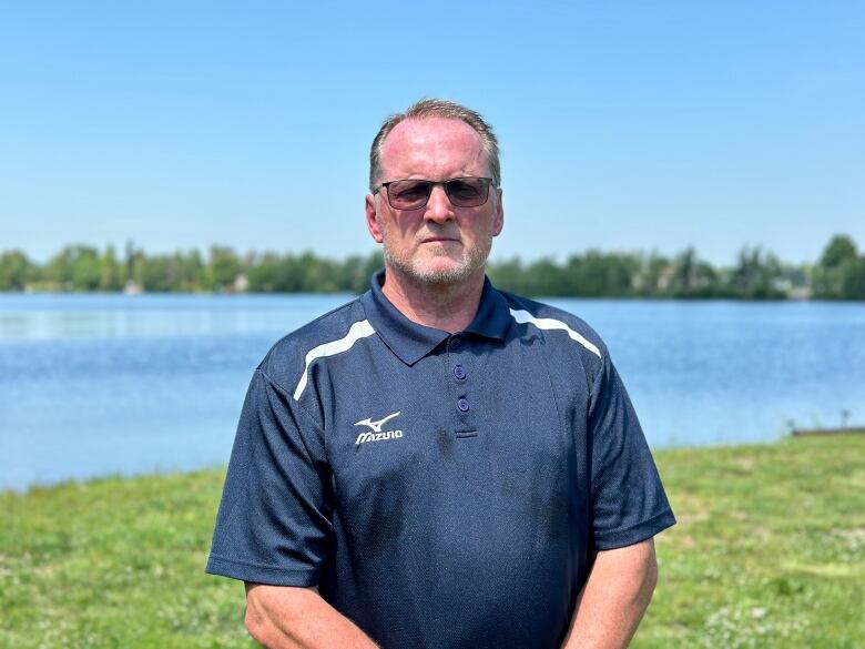 A man stands in front of a lake on a sunny day.