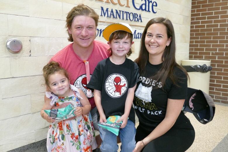 A mom and dad kneel down and pose together with a little boy and little girl.