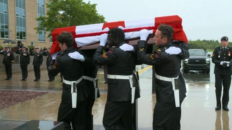 Military members carrying a casket draped with a Canadian flag. 