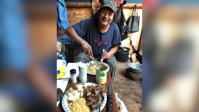 A man sits inside and poses as he eats a meal.