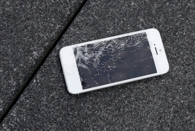 A white iPhone with a smashed screen lays on a sidewalk. 