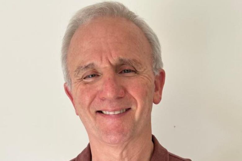 A man standing against a wall smiling. 