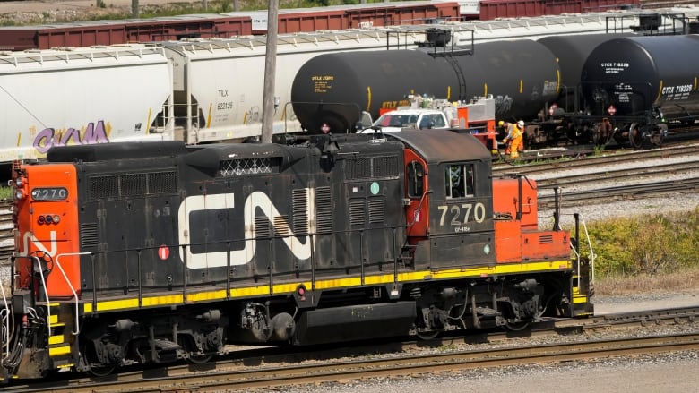 An orange and black train engine in a railyard with the words, CN, painted on it in large white letters