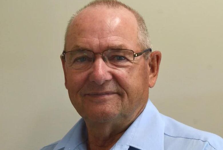 An older man in a blue shirt looks at the camera.