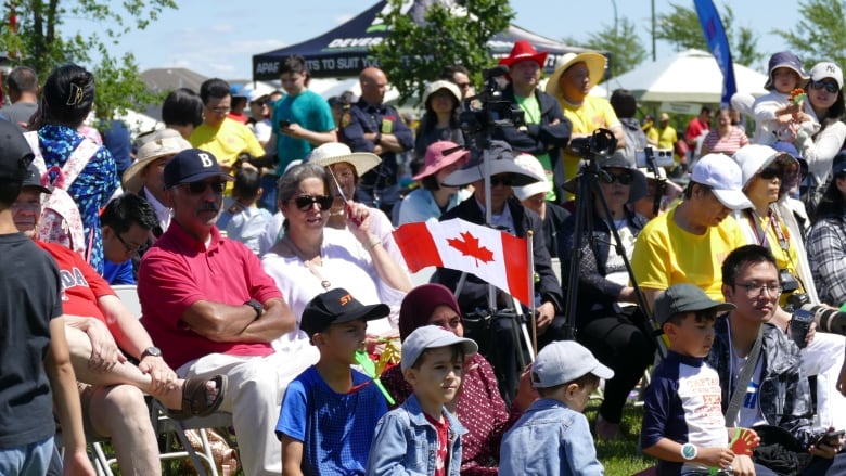 People dressed in red and white for Canada day sit on the grass during an event. 