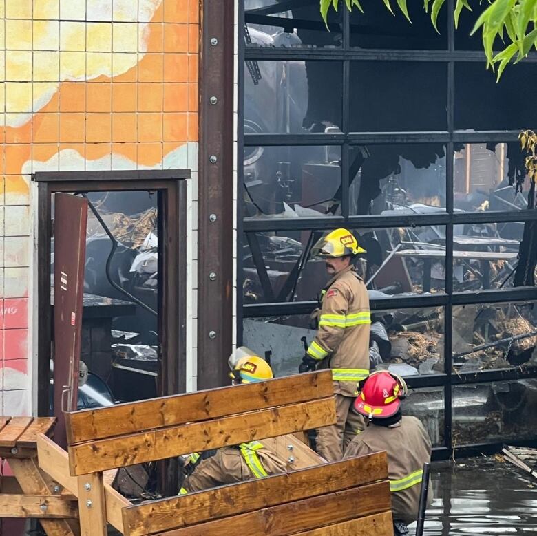 Firemen stand near a dilapidated and burned building.