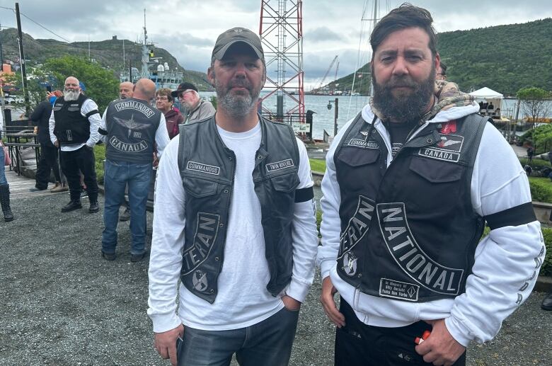 Two men in white t-shirts and leather vests with patches. 