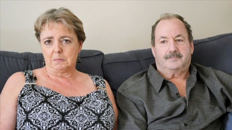 A man and a woman sitting on a couch with stern looks.