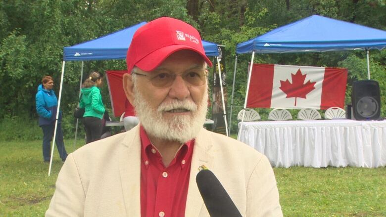 A man with a red shirt and hat stands in front of a microphone. 