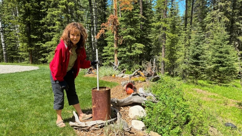 A woman holds a stick poking into the end of a large metal cylinder.  