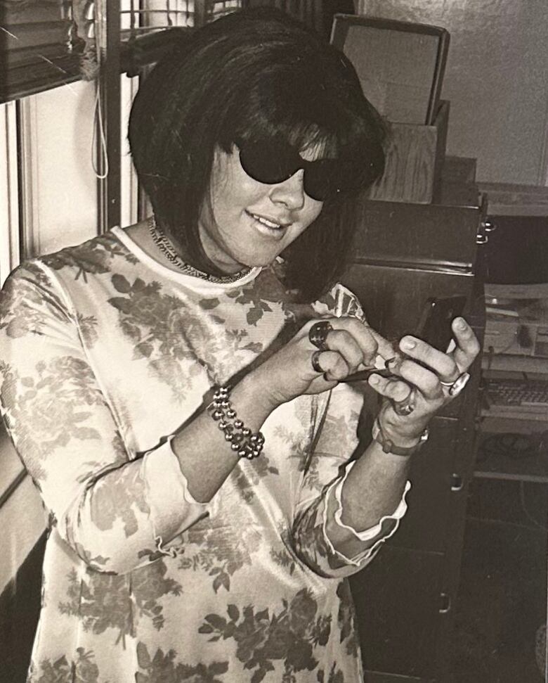 A person in a floral-pattered dress and many rings, wearing sunglasses. 