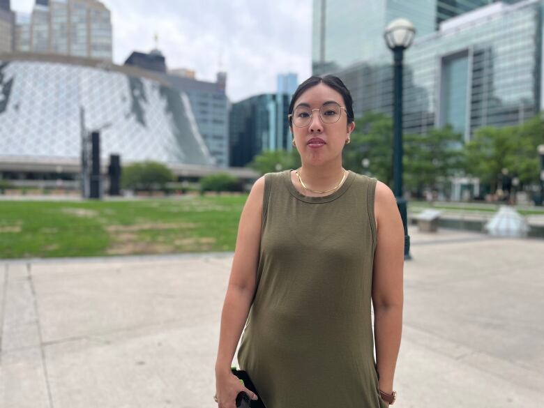 A woman standing in a public square looks at the camera.