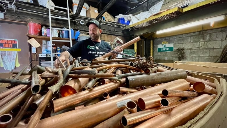 A man wearing a baseball cap and t-shirt poses with a bin of scrap copper.