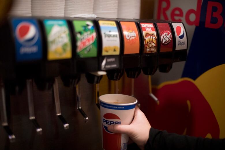 A person holds a pepsi cup under a soft drink dispenser