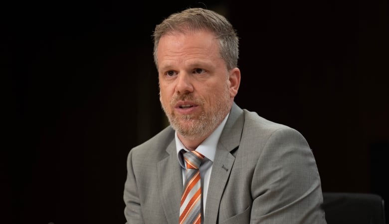 A man wearing a suit looks at the camera.