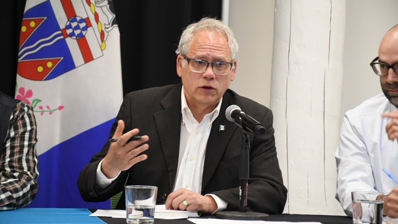 A man in a suit gestures while speaking into a microphone.