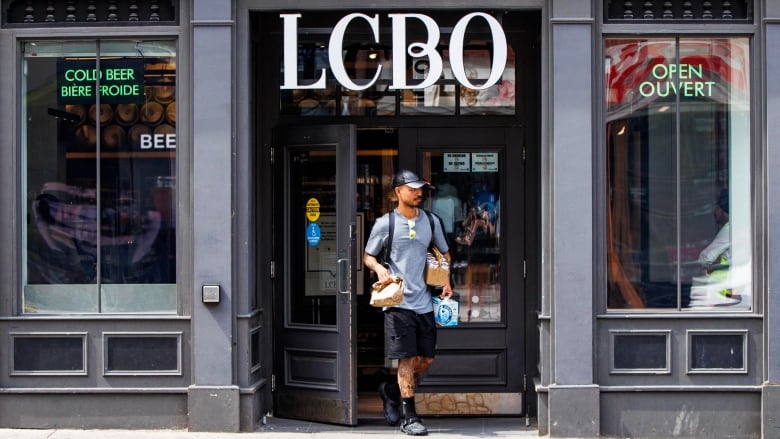 A man leaves a liquor store with alcohol in his hands.