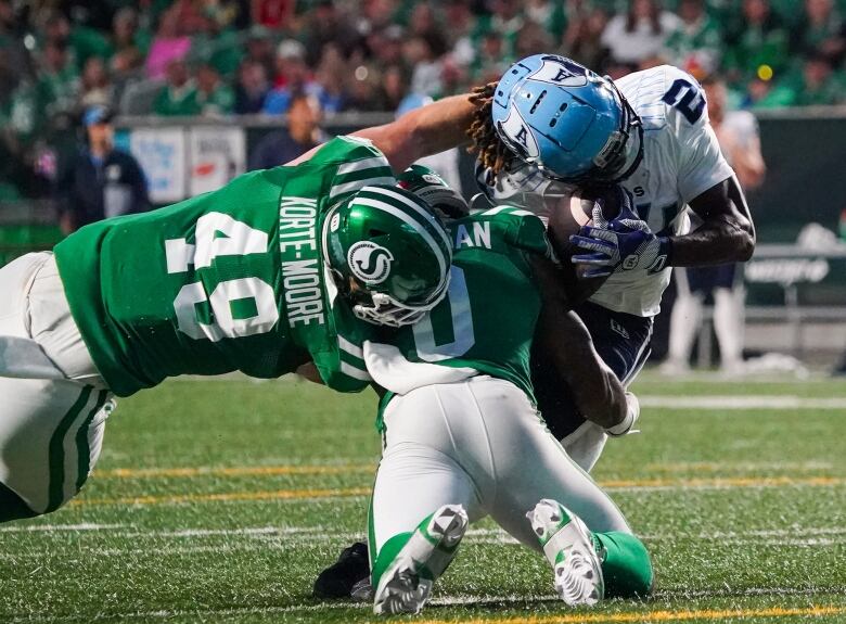 Toronto Argonauts' Deonta McMahon (right) is tackled by Saskatchewan Roughriders' Lake Korte-Moore (49) and Rolan Milligan Jr. (0) during the second half of CFL football action in Regina, on Thursday, July 4, 2024