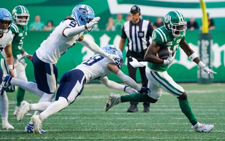 Saskatchewan Roughriders' Samuel Emilus (right) runs past Toronto Argonauts' Royce Metchie (9) and Mason Pierce (28) during the first half of CFL football action in Regina, on Thursday, July 4, 2024.