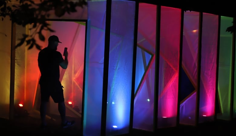 A man walks through a multi-coloured light exhibit where he is cast in silhouette.