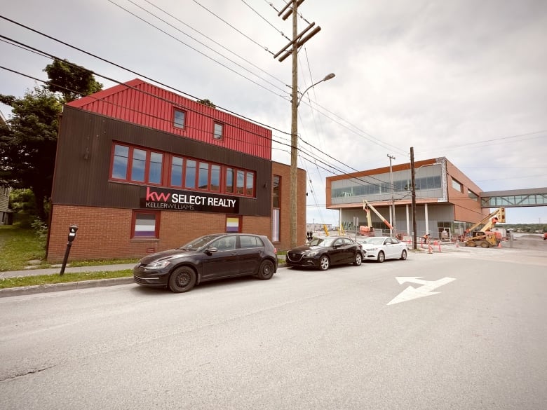 A three-storey red brick building is shown across the street from a new building under construction.