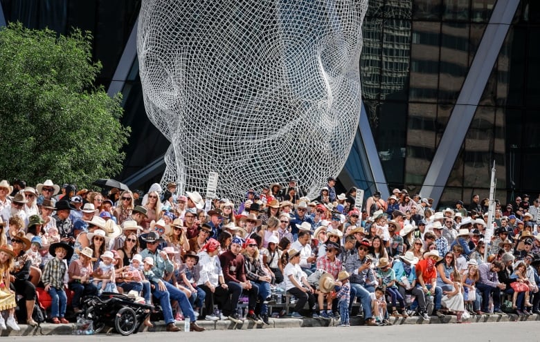 a large sitting crowd lines the street under a wireframe sculpture