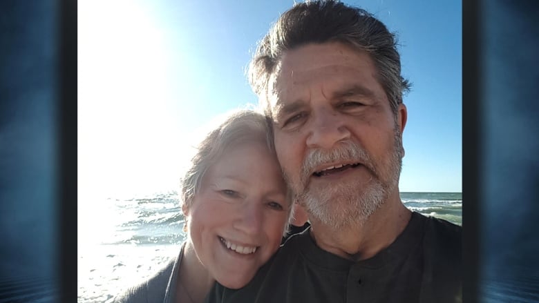 A picture of a woman with grey hair smiling with a man with grey hair and a beard beside her.