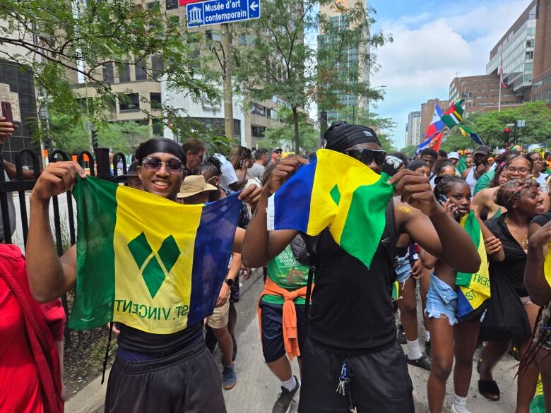 Two men pose for the camera brandishing Saint Vincent and the Grenadines flags. They're part of the Carimas Festival parade in Montreal. 