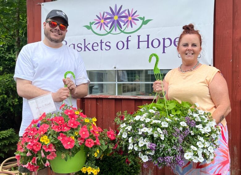 A man and a woman stand next to each other and smile. Each holds up a flower basket.