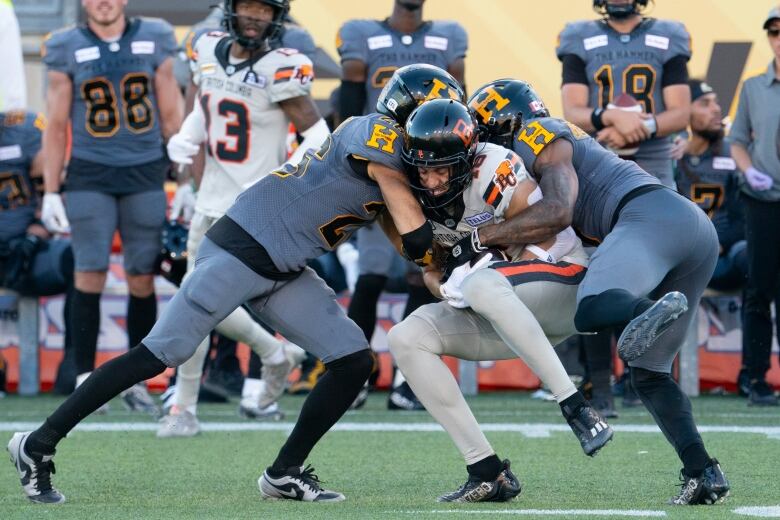 BC Lions Justin McInnis (18) is sandwiched by Hamilton Tiger Cats Destin Talbert (26) and Kenneth George Jr. (3).