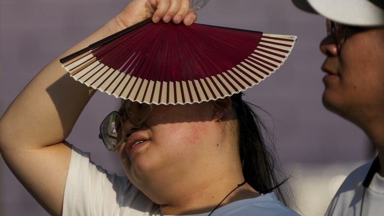 A woman uses a fan as she walks with her companion on a hot day in Beijing in June. June 2024 was the hottest June on record, according to Europe's Copernicus climate service.