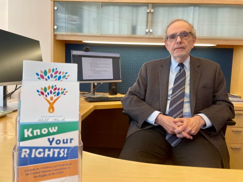 Marvin Bernstein sits at his desk looking at the camera. A pamphlet that says 'know your rights' is seen in the foreground. 