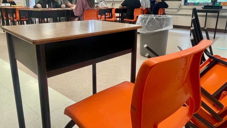 An empty desk is seen with students sitting in other desks in the distance. 