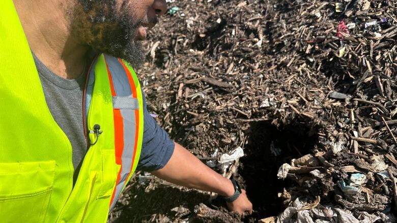 A man in a safety vest with one hand in a pile of compost and garbage.