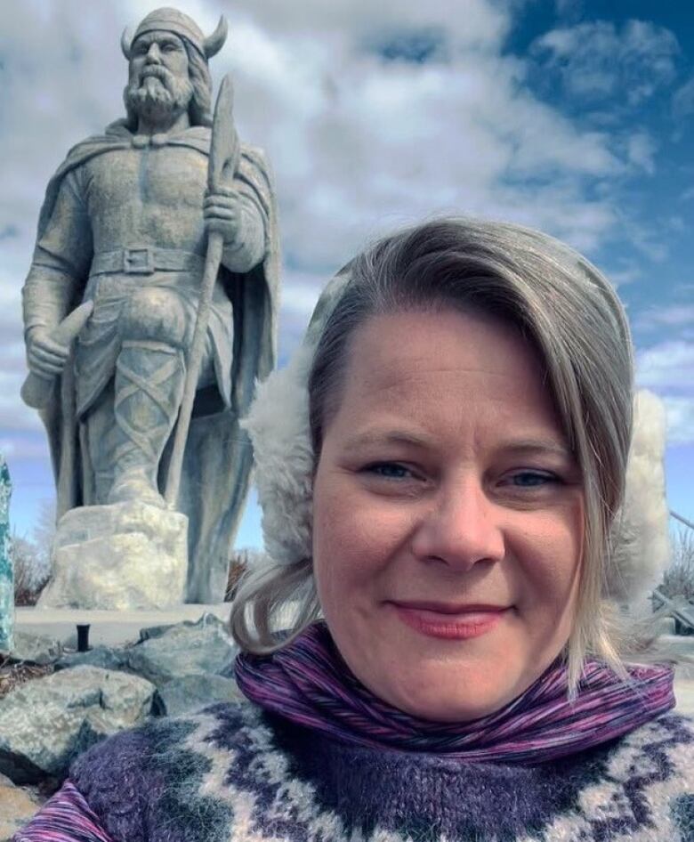 A woman stands in front of a viking statue