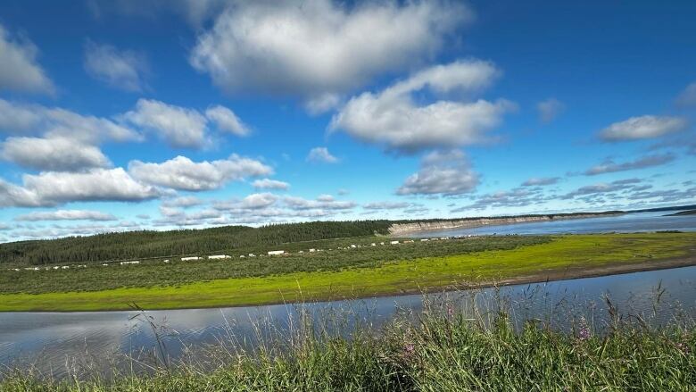 A line of vehicles is seen from afar, across a river.